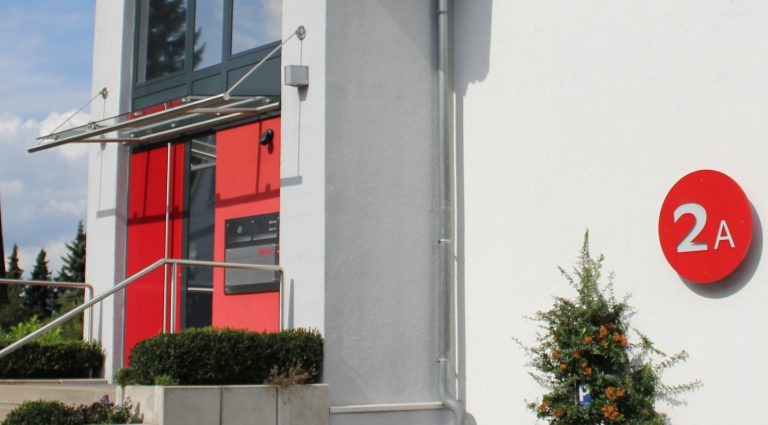 Ein modernes Bürogebäude mit einer roten Hausnummer 2A an der Fassade. Ein modernes Bürogebäude mit einer roten Hausnummer 2A an der Fassade.<br />